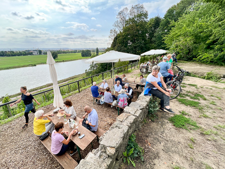 Mensen proeven wijn op een terras tussen de wijngaarden, met zicht op de Elbe bij Dresden.